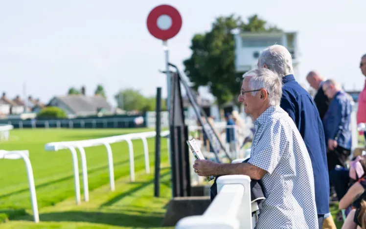 A race goer holding a race card looks out over the track at Great Yarmouth